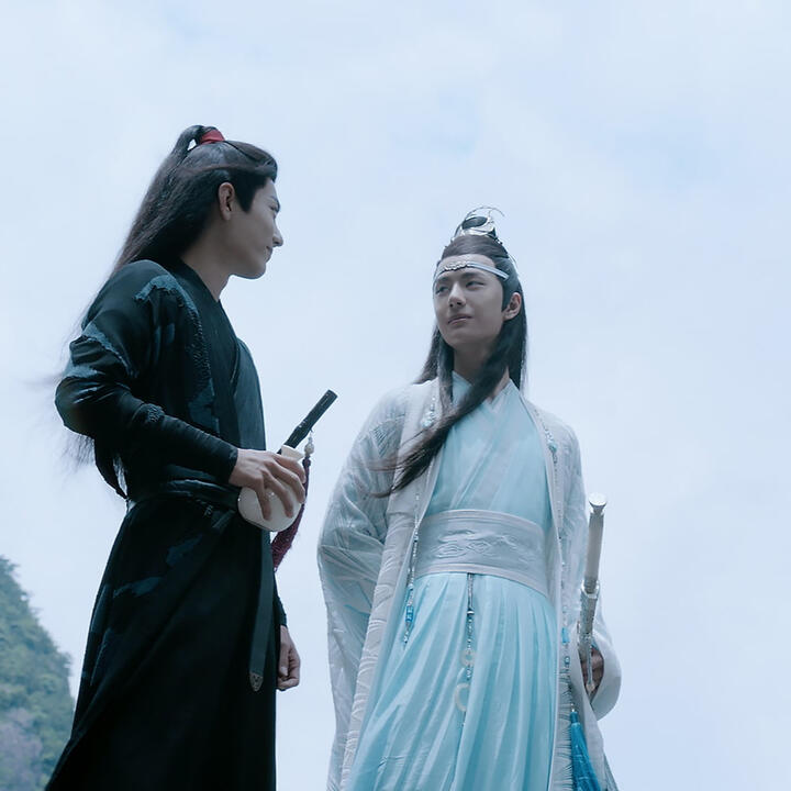 wei wuxian and lan wangji smile at each other, silhouetted against a clear blue sky.