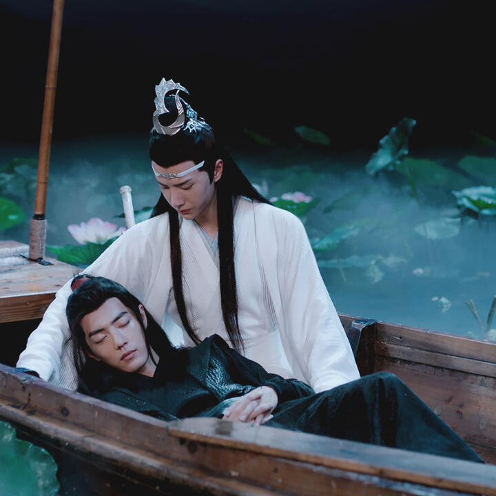 in a lake filled with lotuses, wei wuxian lies on lan wangji’s lap in a boat.
